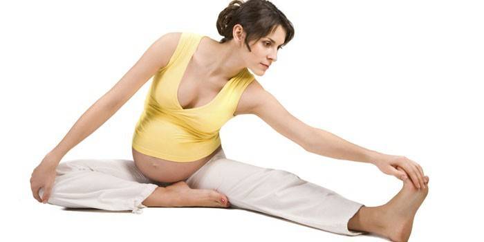 Беременная девушка делает упражнение на растяжку
