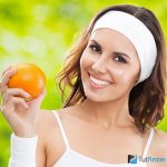 Спортивная девушка держит в руке апельсин